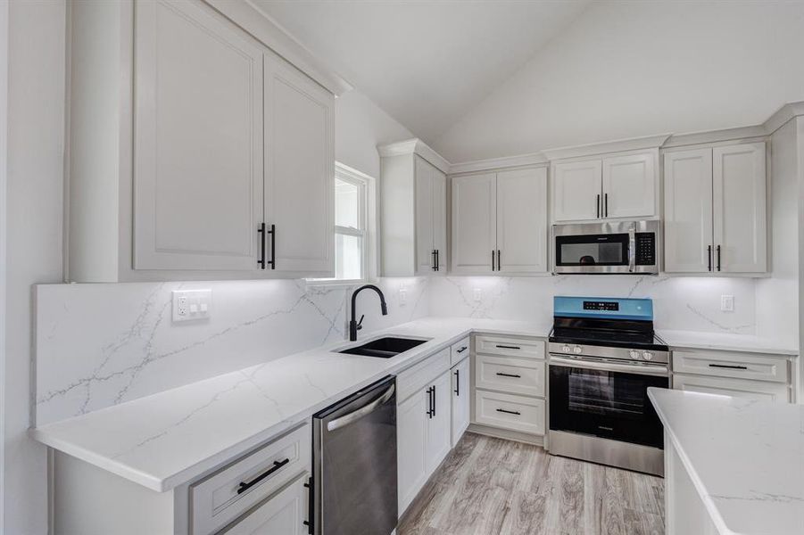 Kitchen featuring white cabinets, sink, lofted ceiling, and stainless steel appliances