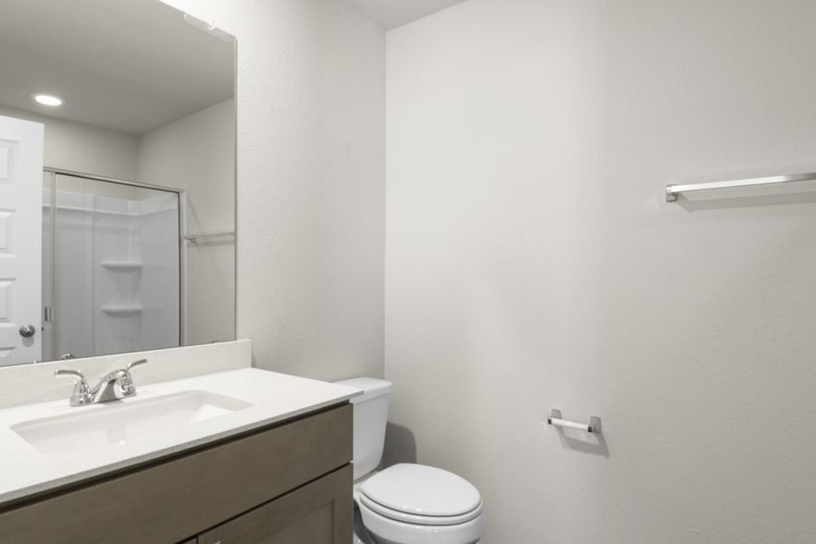 Image of a primary bathroom with light grey walls, brown cabinets, a white vanity and a large mirror