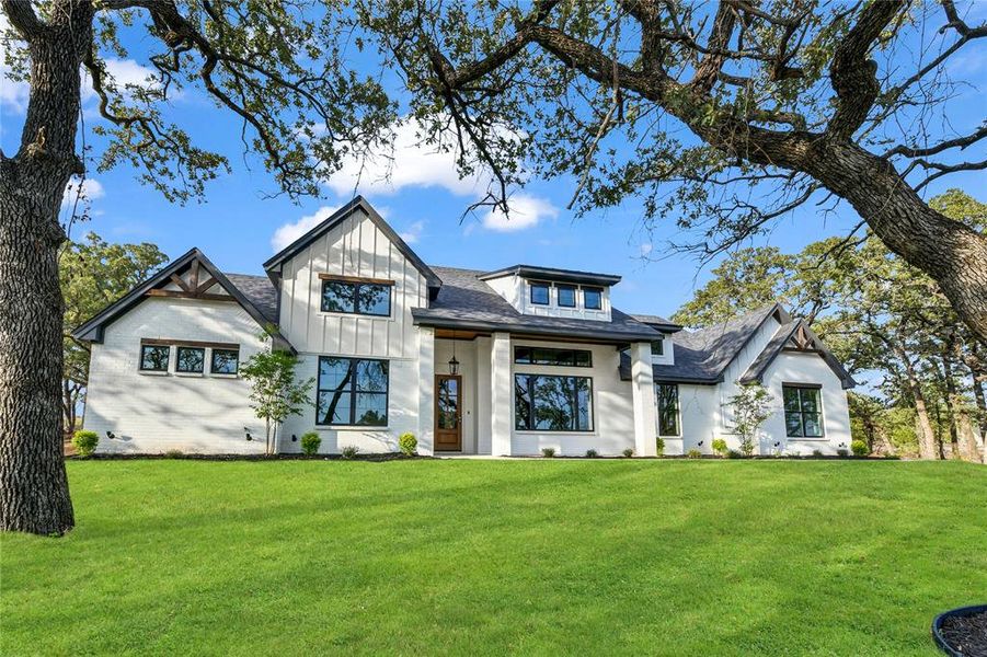 Modern farmhouse style home featuring board and batten siding, roof with shingles, and a front yard Modern farmhouse style home featuring board and batten siding, roof with shingles, and a front yard