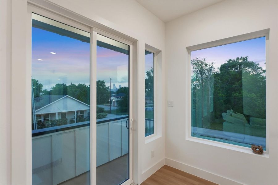 Bright corner living space featuring oversized windows and sliding glass doors that flood the room with natural light and provide direct access to a private balcony with neighborhood and skyline views.