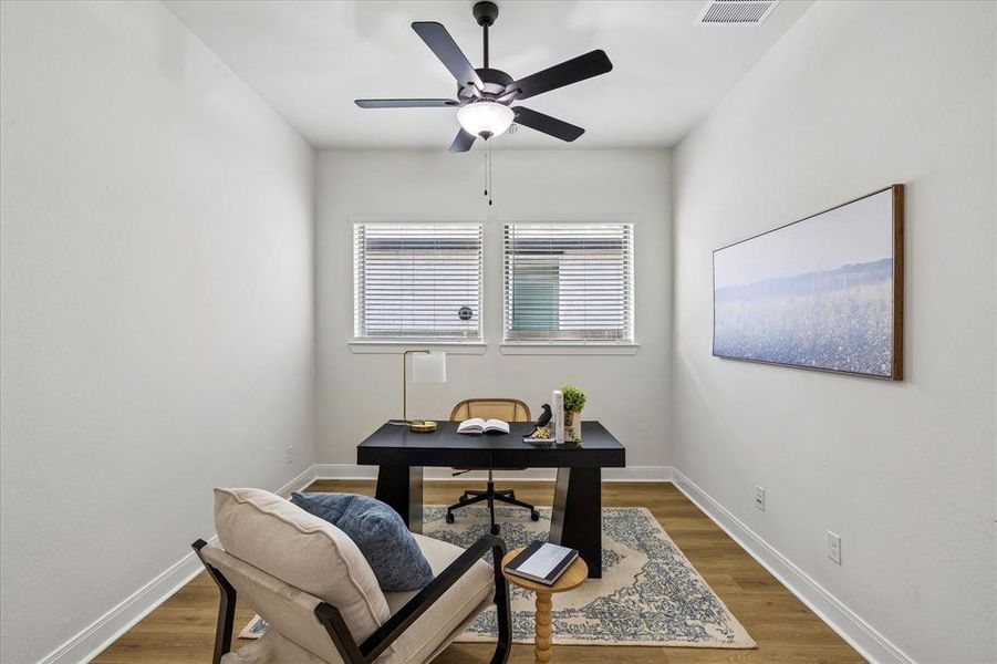 Bright room with wood-finish flooring, two windows with blinds, a ceiling fan with integrated lighting, and white baseboards Bright room with wood-finish flooring, two windows with blinds, a ceiling fan with integrated lighting, and white baseboards