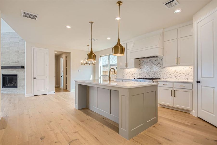 Kitchen featuring hanging light fixtures, light hardwood / wood-style floors, a fireplace, and an island with sink