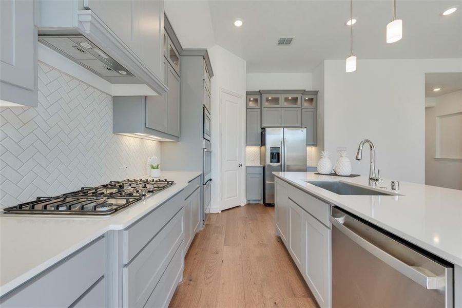 Kitchen with pendant lighting, sink, light hardwood / wood-style flooring, tasteful backsplash, and stainless steel appliances