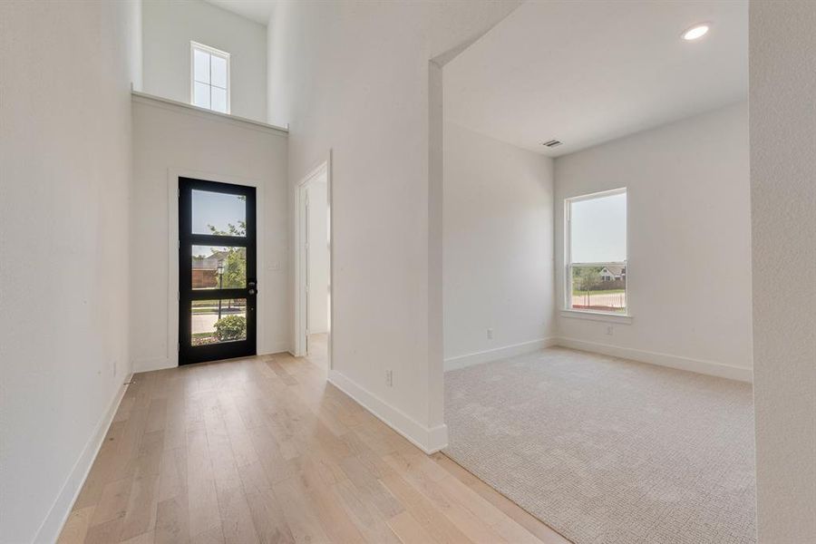 Foyer featuring light wood finished floors, a towering ceiling, recessed lighting, and light carpet Foyer featuring light wood finished floors, a towering ceiling, recessed lighting, and light carpet