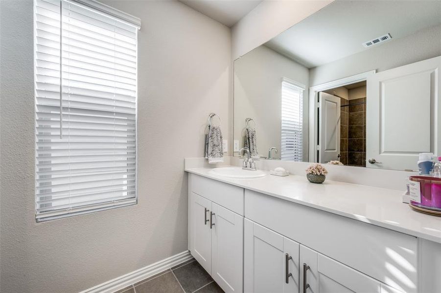 Bathroom featuring dark tile patterned floors, vanity, a textured wall, and a shower Bathroom featuring dark tile patterned floors, vanity, a textured wall, and a shower