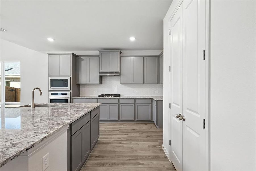 Kitchen with gray cabinetry, appliances with stainless steel finishes, recessed lighting, light wood finished floors, and under cabinet range hood Kitchen with gray cabinetry, appliances with stainless steel finishes, recessed lighting, light wood finished floors, and under cabinet range hood