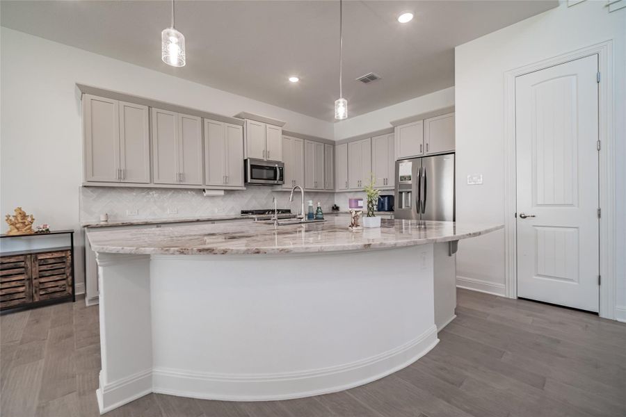An inviting kitchen with light wood flooring offers ample granite countertop space and modern stainless steel appliances.