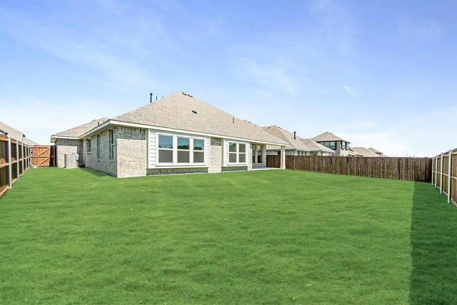Expansive backyard with a manicured lawn, full privacy fencing, and a light brick exterior Expansive backyard with a manicured lawn, full privacy fencing, and a light brick exterior