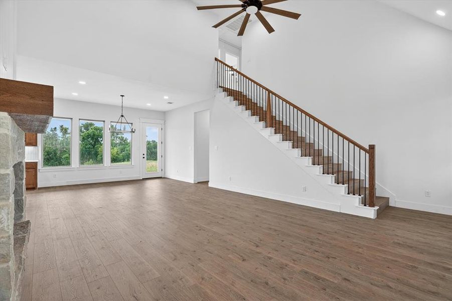 Spacious living area featuring wood-finish flooring, a prominent stone-clad fireplace with a wood mantle, and a staircase with wood handrails and black iron balusters