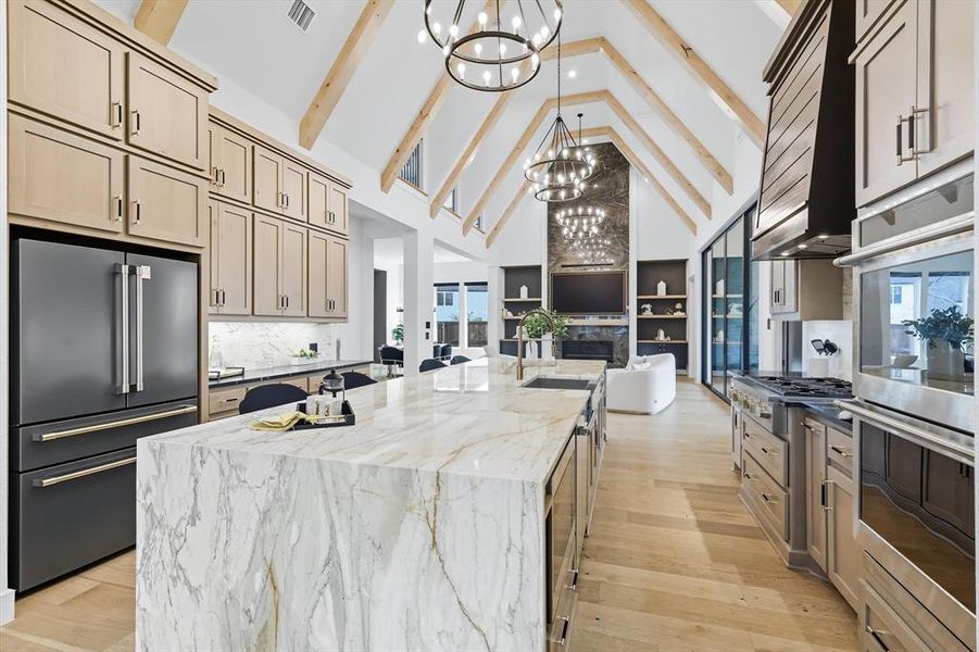 Kitchen with high vaulted ceiling, stainless steel appliances, a fireplace, beamed ceiling, and light hardwood floors Kitchen with high vaulted ceiling, stainless steel appliances, a fireplace, beamed ceiling, and light hardwood floors