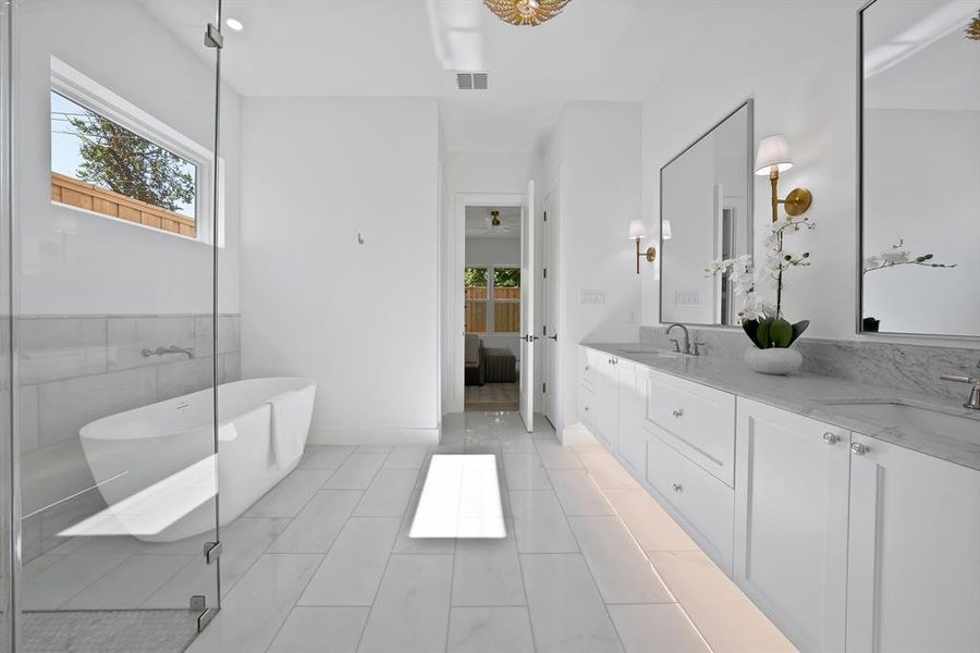 Bathroom featuring a freestanding soaking tub, frameless glass shower enclosure, and a long dual-sink vanity with under-cabinet lighting