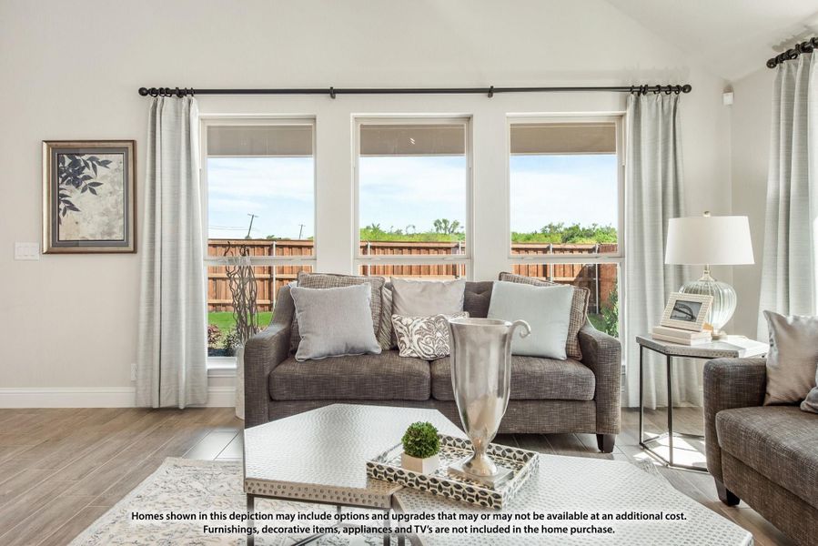 Living room with gray sofa, coffee table, and three large windows with backyard view Living room with gray sofa, coffee table, and three large windows with backyard view
