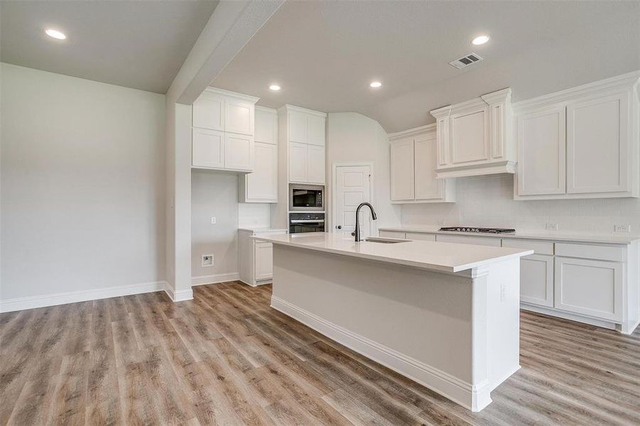 Kitchen featuring white cabinetry, stainless steel appliances, light hardwood / wood-style floors, and an island with sink