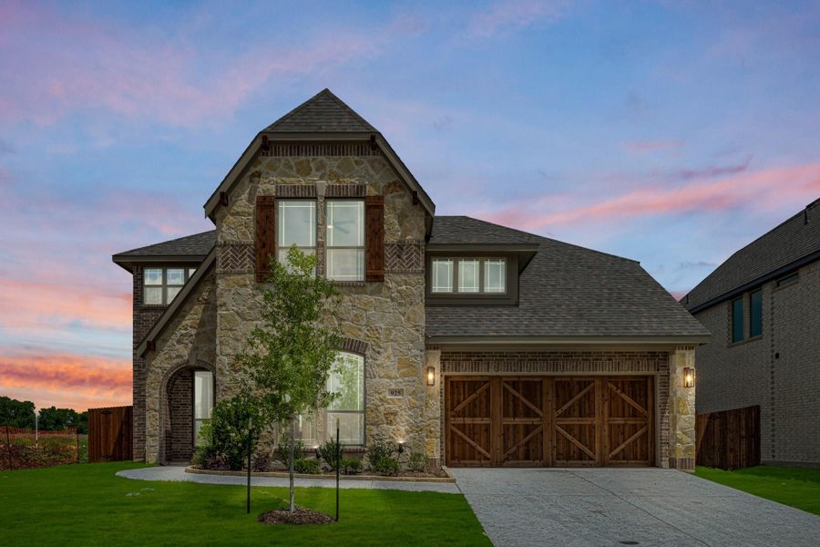 Two-story home with stone and brick exterior, wood garage doors, arched entry, and green front lawn at dusk Two-story home with stone and brick exterior, wood garage doors, arched entry, and green front lawn at dusk