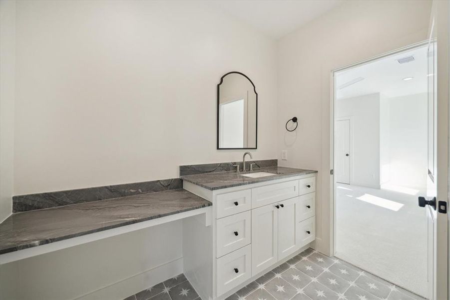 A thoughtfully designed ensuite bathroom offers both style and functionality, conveniently shared with the adjacent game room. A custom vanity features clean lines, ample storage, and a sleek stone countertop, complemented by a built-in makeup or workspace.