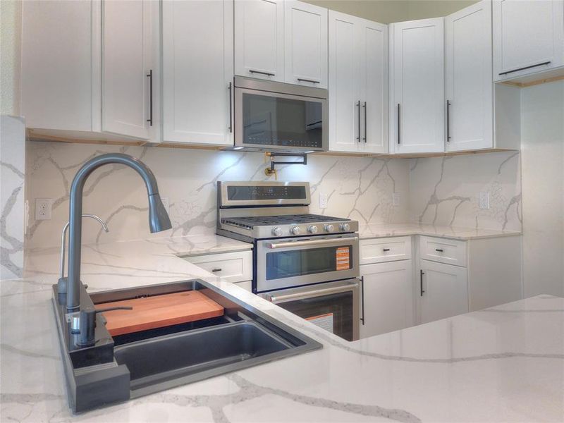 Modern kitchen featuring white shaker cabinetry with dark hardware, a stainless steel range with double ovens, a built-in microwave, and integrated countertops and backsplash with visible veining