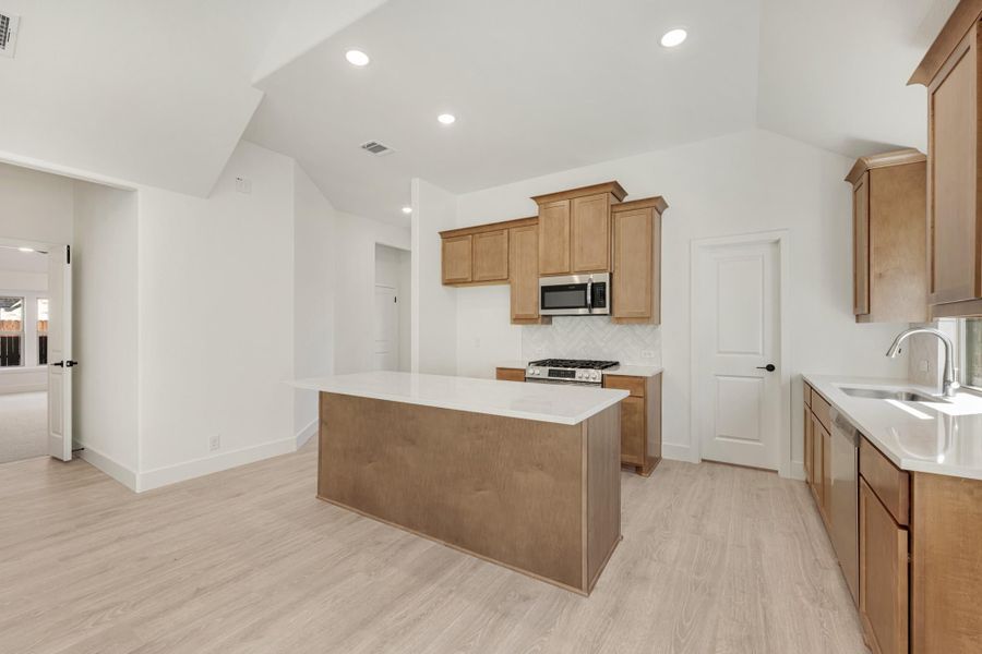 Kitchen with center island, wood cabinets, stainless steel appliances, and light hardwood floors under vaulted ceiling