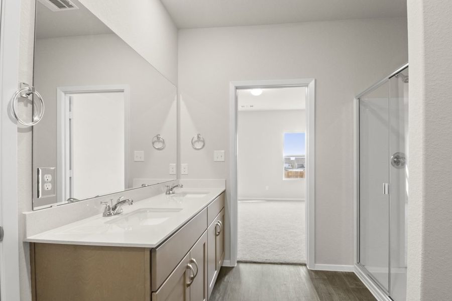 Image of a primary bedroom with light brown cabinets, a white double vanity, a large mirror, and a standing shower