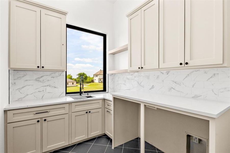 Utility room featuring shaker-style cabinetry, white countertops, marble-look subway tile backsplash, and a large black-framed window