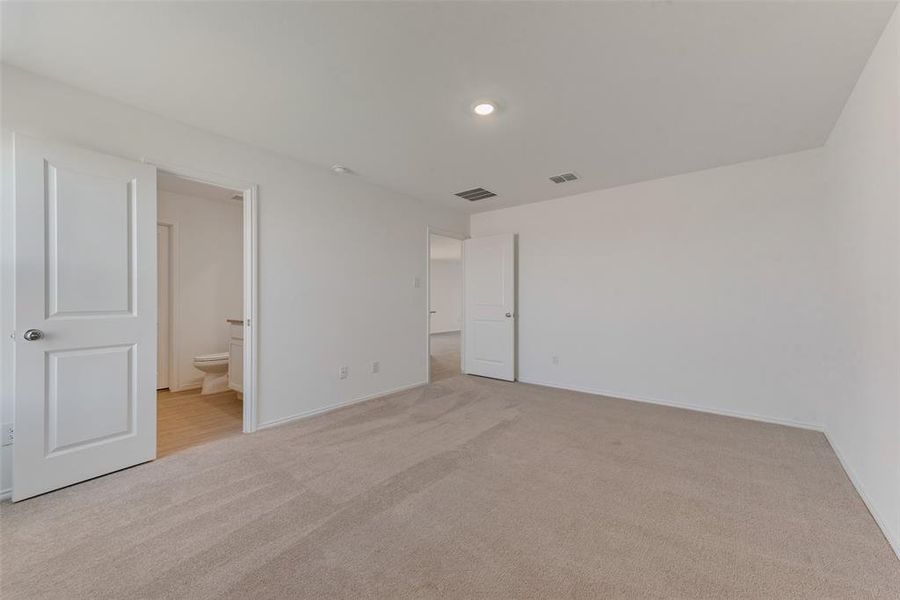 Unfurnished bedroom with light colored carpet and connected bathroom