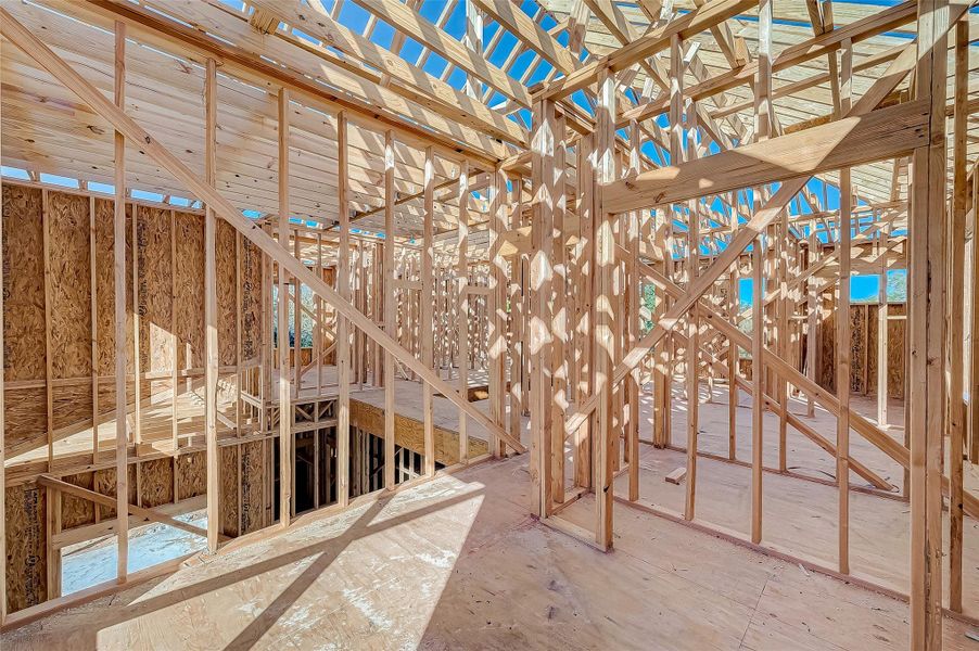This photo shows the interior framing of a house under construction, highlighting the wooden studs and beams. The structure is open to the sky, indicating early stages of development.