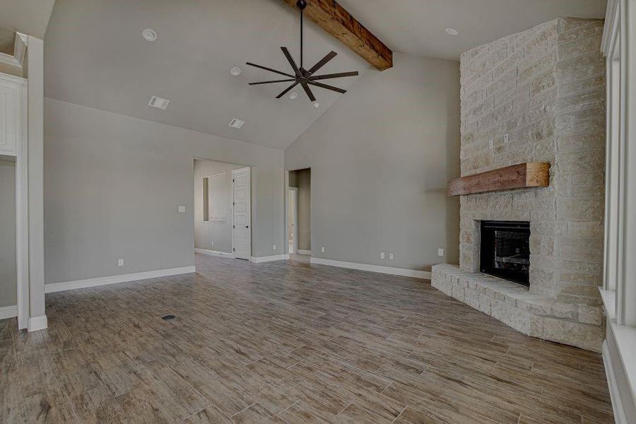 Unfurnished living room featuring a fireplace, light wood-type flooring, ceiling fan, high vaulted ceiling, and beam ceiling