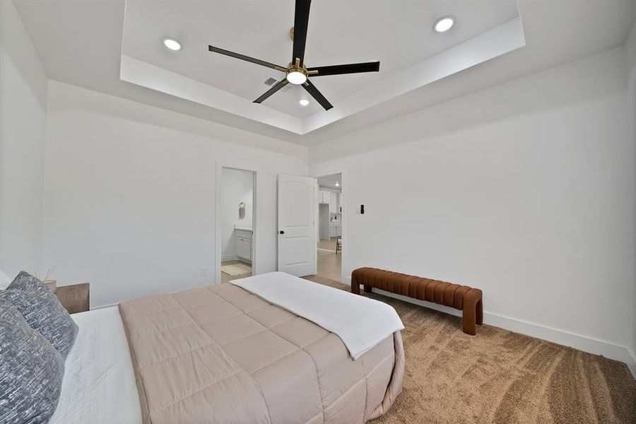 Primary Bedroom with recessed lighting, a raised ceiling, light carpet, ensuite bathroom, and ceiling fan