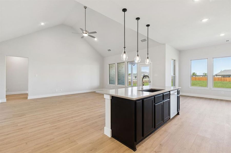 Kitchen with dark cabinetry, open floor plan, light wood finished floors, an island with sink, and hanging light fixtures