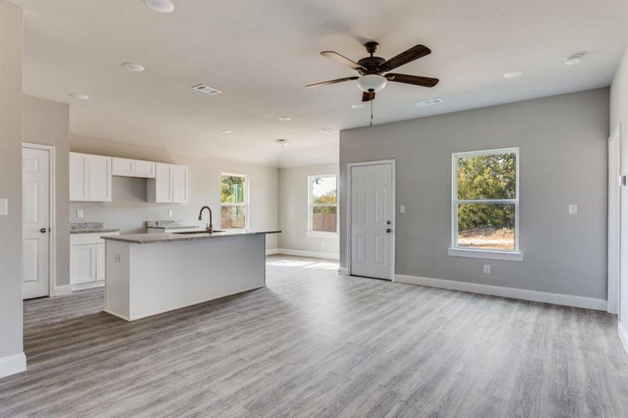 Kitchen featuring white cabinetry, an island with sink, light stone countertops, a ceiling fan, and light wood-style flooring