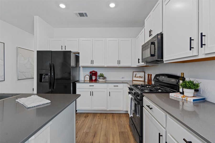 Kitchen featuring black appliances, light wood-type flooring, white cabinetry, dark countertops, and recessed lighting