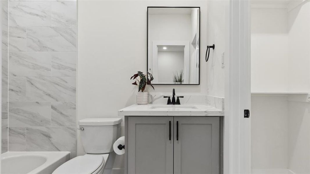 This bathroom features a sleek, modern design with a marble-tiled shower and tub combo. It has a stylish vanity with a marble countertop, black fixtures, and a large mirror. The neutral color palette and minimalist decor create a clean, inviting space.