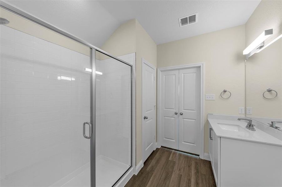 Contemporary bathroom featuring a glass-enclosed shower with subway tile, wood-finish flooring, a white vanity with an integrated sink, and double bi-fold doors