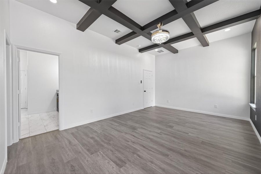 Luxurious primary bedroom featuring generous space, abundant natural light, and stunning custom wood ceiling beams that add warmth, character, and an elegant designer touch.