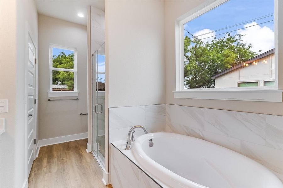 Full bath with plenty of natural light, a shower stall, a bath, and wood finished floors