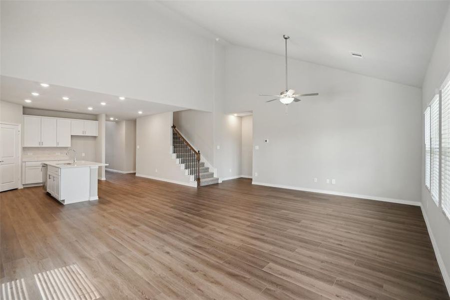 Unfurnished living room with sink, light hardwood / wood-style flooring, ceiling fan, and high vaulted ceiling