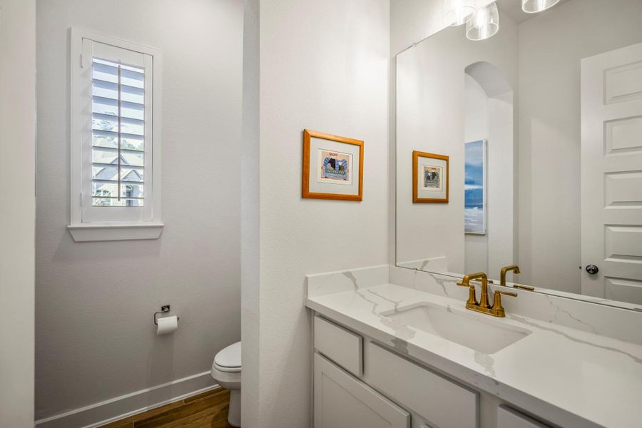 This half bath near the office features a modern design with a white marble countertop and gold faucet.