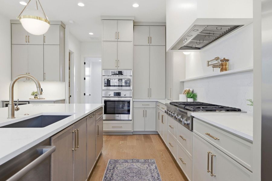 Kitchen with two tone cabinets, decorative light fixtures, stainless steel appliances, light wood-type flooring, and light stone countertops