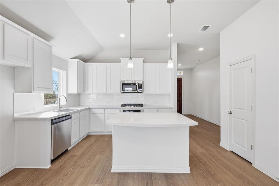 Kitchen with white cabinets, a center island, appliances with stainless steel finishes, decorative light fixtures, and light wood-style floors