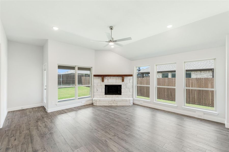 Living room with stone fireplace, hardwood floors, ceiling fan, and large windows overlooking backyard Living room with stone fireplace, hardwood floors, ceiling fan, and large windows overlooking backyard