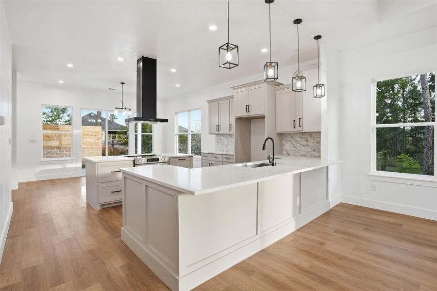 Kitchen featuring a peninsula, range hood, light wood-style flooring, and decorative light fixtures