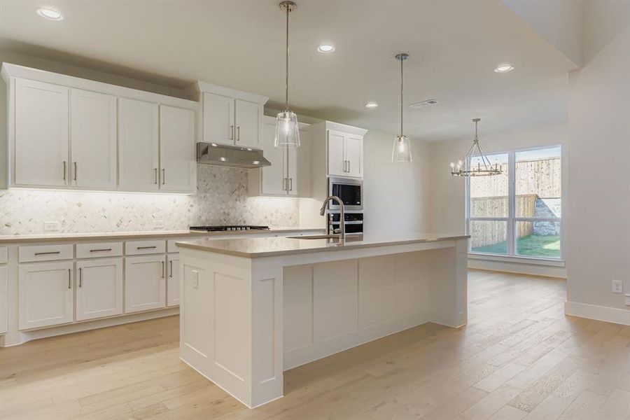 Kitchen with tasteful backsplash, recessed lighting, white cabinetry, light wood-style flooring, and a kitchen island with sink