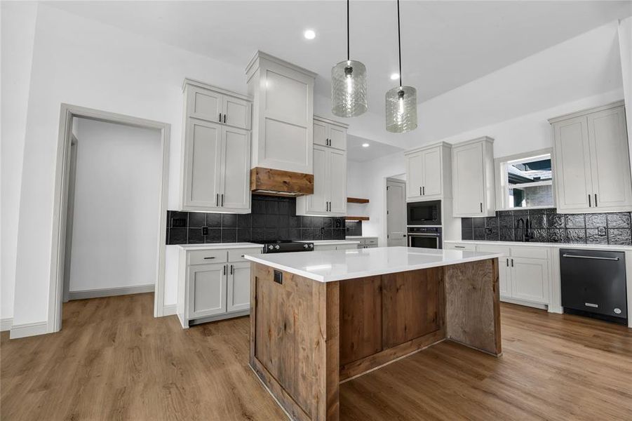 Kitchen with sink, decorative light fixtures, light hardwood / wood-style flooring, appliances with stainless steel finishes, and a center island