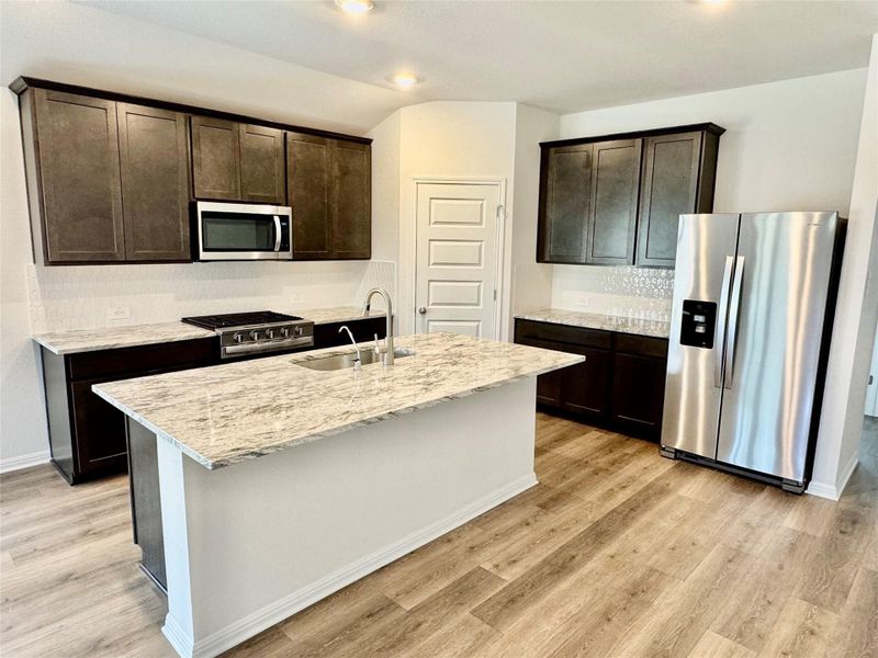 Kitchen featuring appliances with stainless steel finishes, dark brown cabinetry, a kitchen island with sink, and light wood-type flooring Kitchen featuring appliances with stainless steel finishes, dark brown cabinetry, a kitchen island with sink, and light wood-type flooring