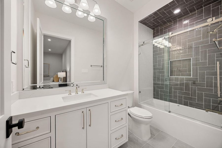 This bathroom combines clean design with functional elegance, featuring a large vanity, ample storage, and bright lighting throughout. The neutral palette creates a timeless look that feels fresh and inviting. The highlight of this space is the tiled tub-shower combo with sleek glass enclosure and detailed tile work, offering both practicality and a polished, modern finish.