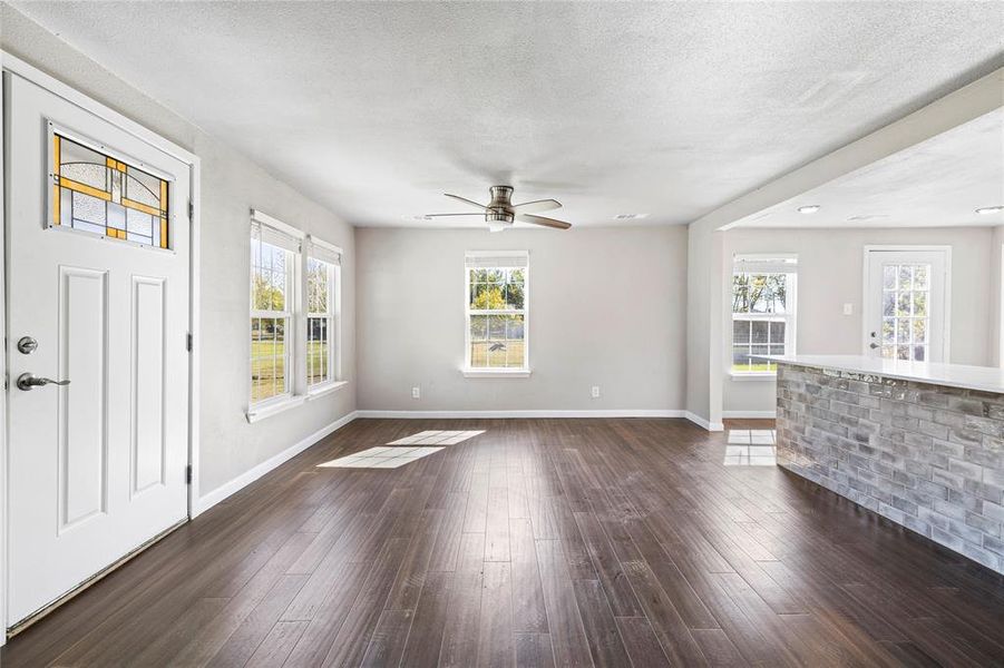 Unfurnished living room with a textured ceiling, dark wood finished floors, and a ceiling fan