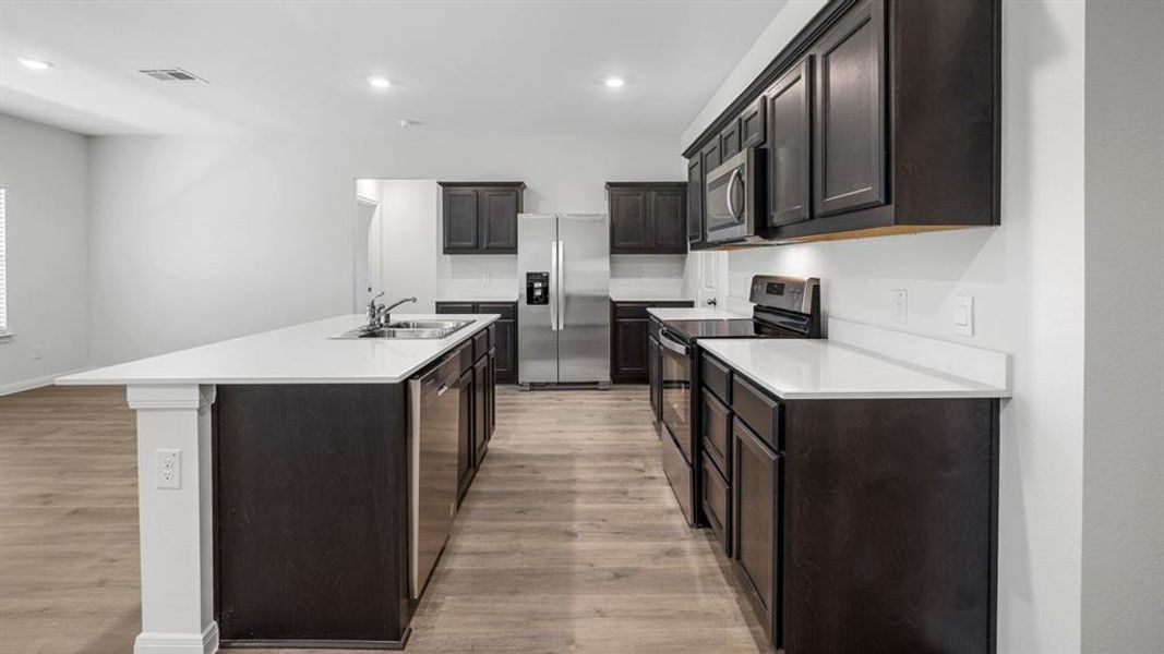 Kitchen with stainless steel appliances, a kitchen island with sink, recessed lighting, and light wood finished floors