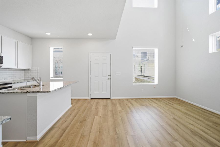 Kitchen featuring light stone countertops, white cabinetry, light wood finished floors, decorative backsplash, and a center island with sink