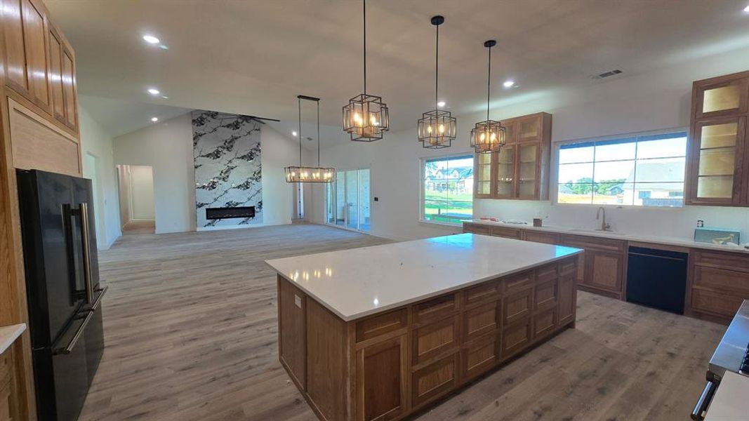 Kitchen featuring brown cabinetry, open floor plan, a kitchen island, high end black fridge, and decorative light fixtures