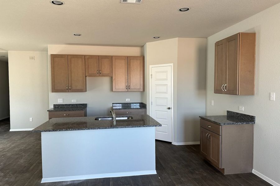 Image of home kitchen with light brown cabinets, center island, wood-look floors, and white walls