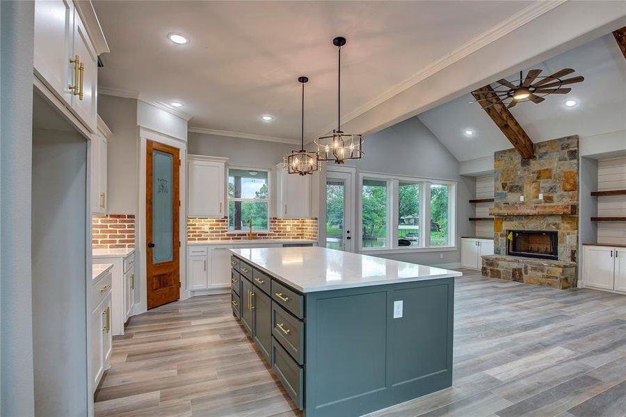 Kitchen featuring decorative light fixtures, a fireplace, ceiling fan with notable chandelier, white cabinets, and a center island